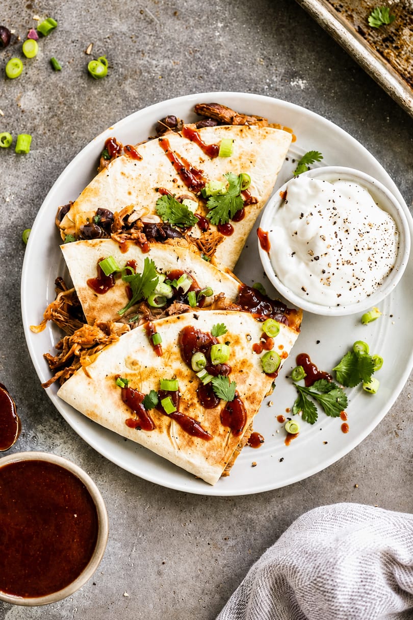 Pulled pork quesadillas with black beans, BBQ sauce, cilantro, and green onions, served with sour cream.