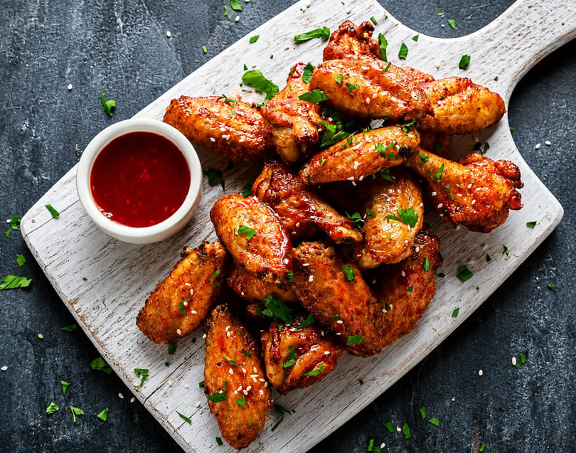 Glazed chicken wings with sesame seeds and parsley, served with a side of red dipping sauce.