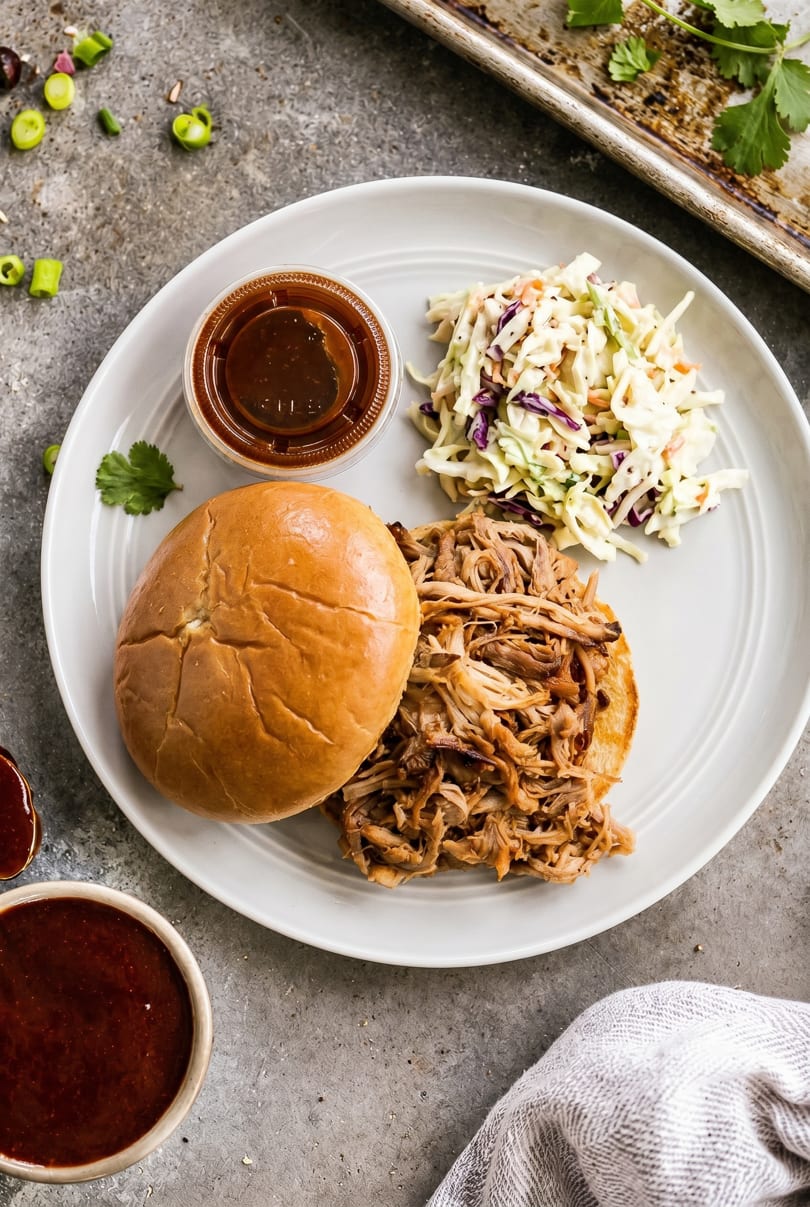 Pulled pork sandwich with coleslaw and barbecue sauce on a white plate, overhead view.