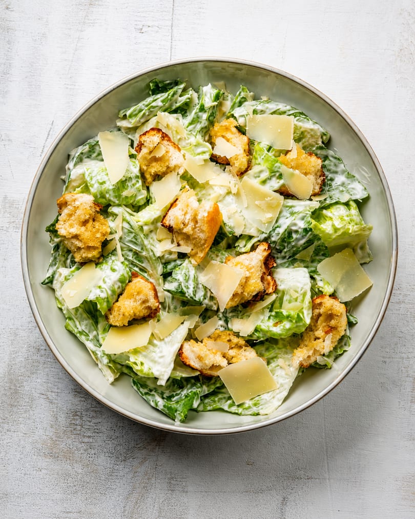 Caesar salad with romaine lettuce, creamy dressing, croutons, and parmesan cheese in a bowl.